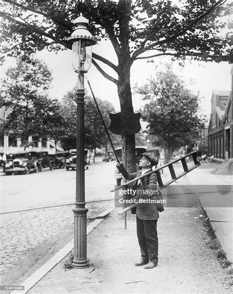 A Lamplighter Carries A Ladder As He Lights The Gas Street Lamps
