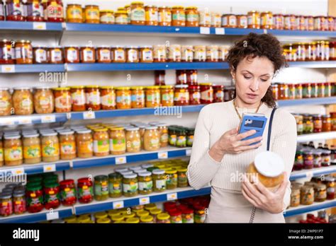 Female Shopper Scans Barcode On Jar Of Sauerkraut Using A Smartphone Female Shopper Scans Barcode On Jar Of Sauerkraut Using A Smartphone