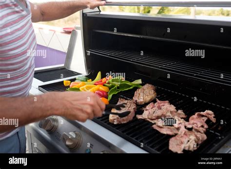 Man Barbecuing Steak And Different Kinds Of Peppers On A Gas Grill Man Barbecuing Steak And Different Kinds Of Peppers On A Gas Grill